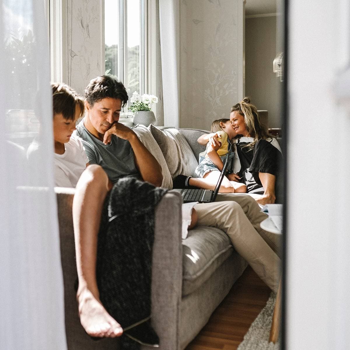 En familj med mamma, pappa och två små barn sitter i en soffa i ett vardagsrum.