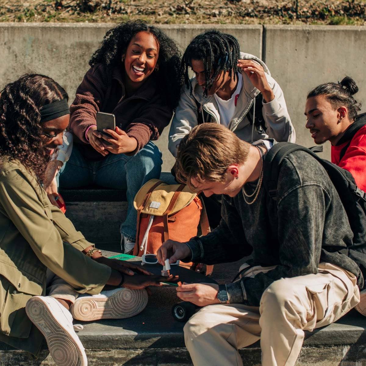 Glada tjejer och killar umgås sittande i park.