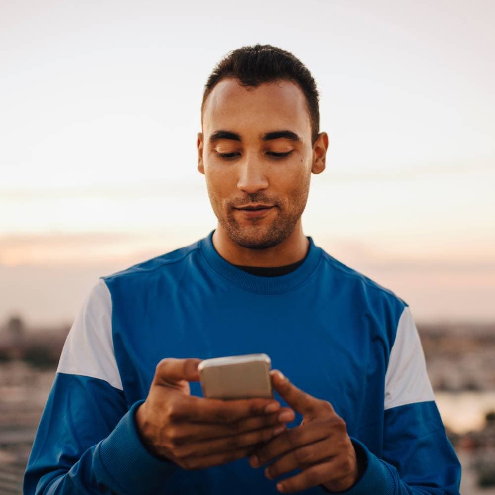 En kille med kort mörkt hår och blå tröja tittar småleende ner på sin telefon